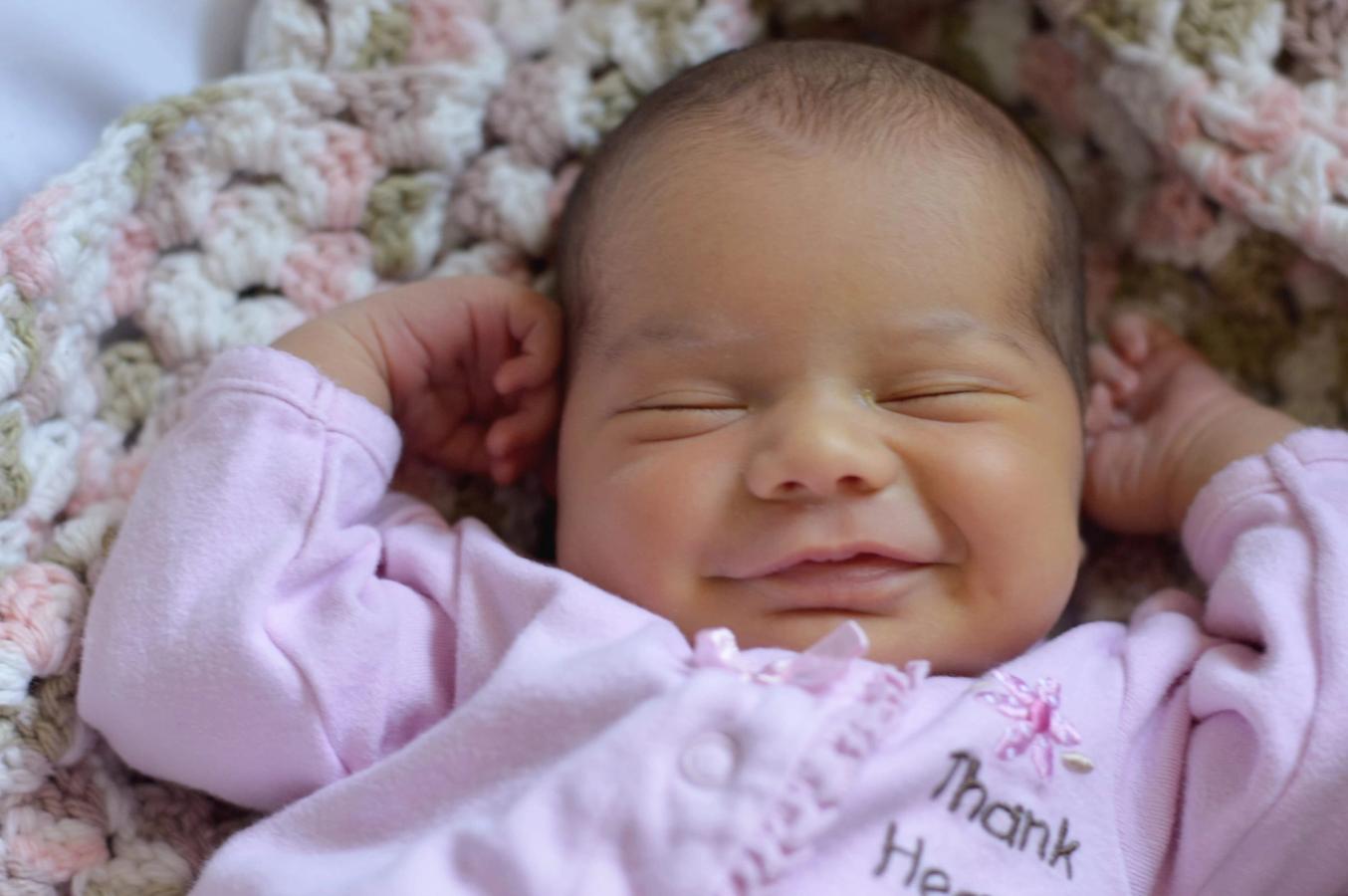 A sleeping newborn baby wrapped in a pink crocheted blanket, close-up portrait.