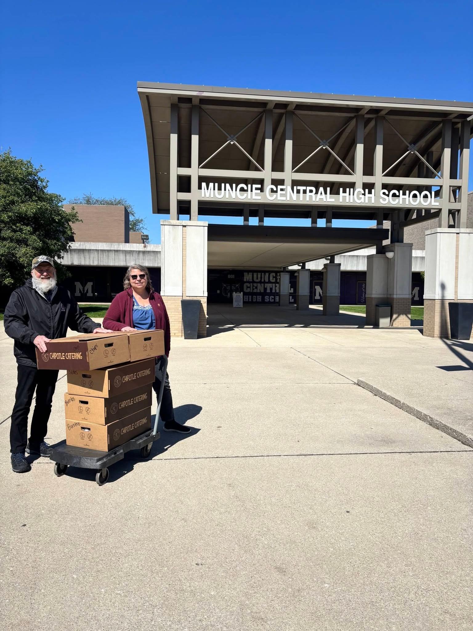 Two church volunteers wheel a cart of catered lunches up to Muncie Central High School