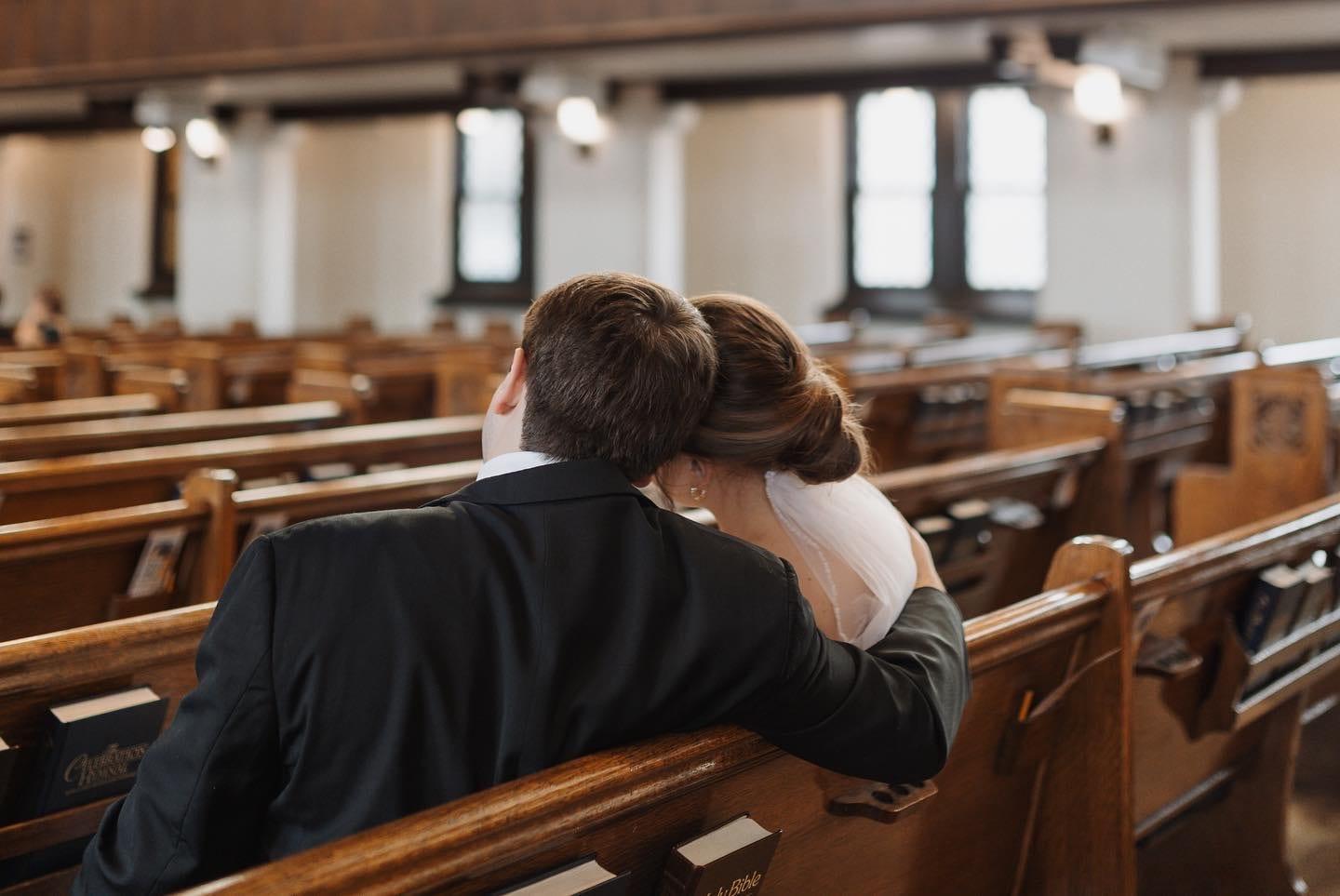 A bride and groom share a kiss, seated in a sanctuary pew