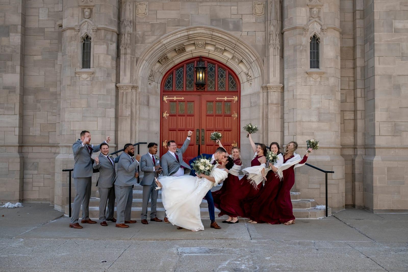 A wedding party celebrating in front of the church's red doors