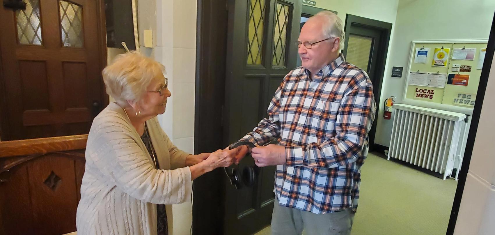 At the sanctuary door, a man hands a woman a set of assisted-listening headphones.