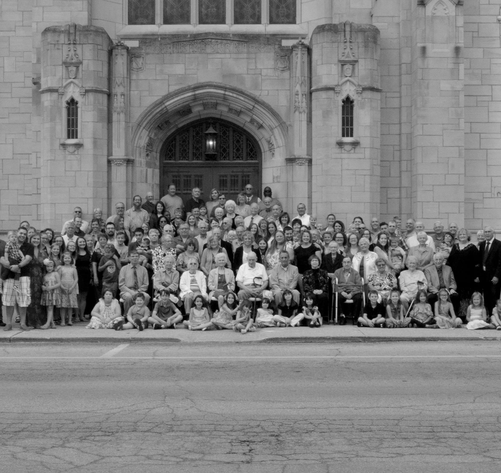 The congregation, adults and children, gathered outside the church entrance in a black and white photograph.