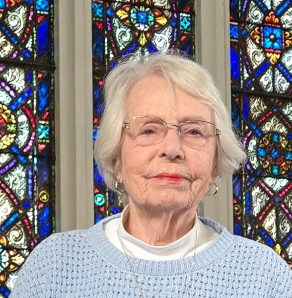 Nina Oisten, an older woman with glasses, in front of a stained glass window.