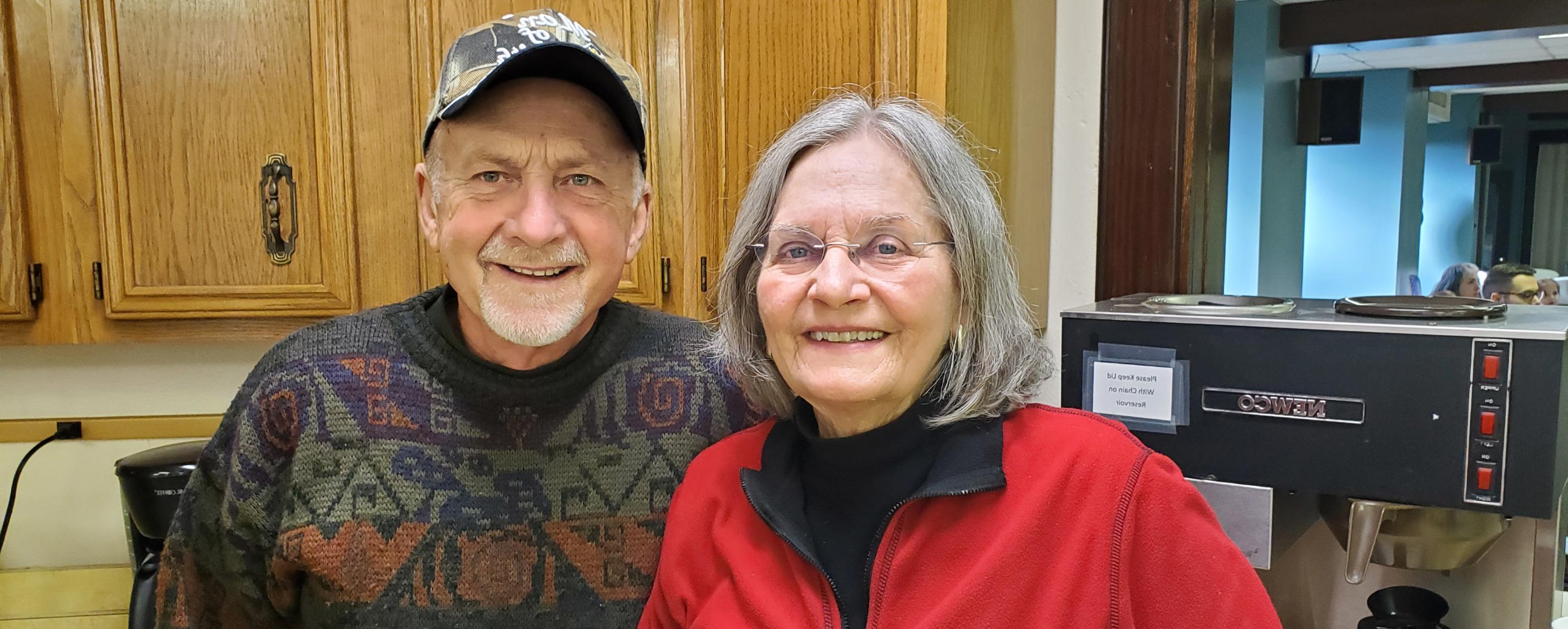An older man and woman posing together in a kitchen.