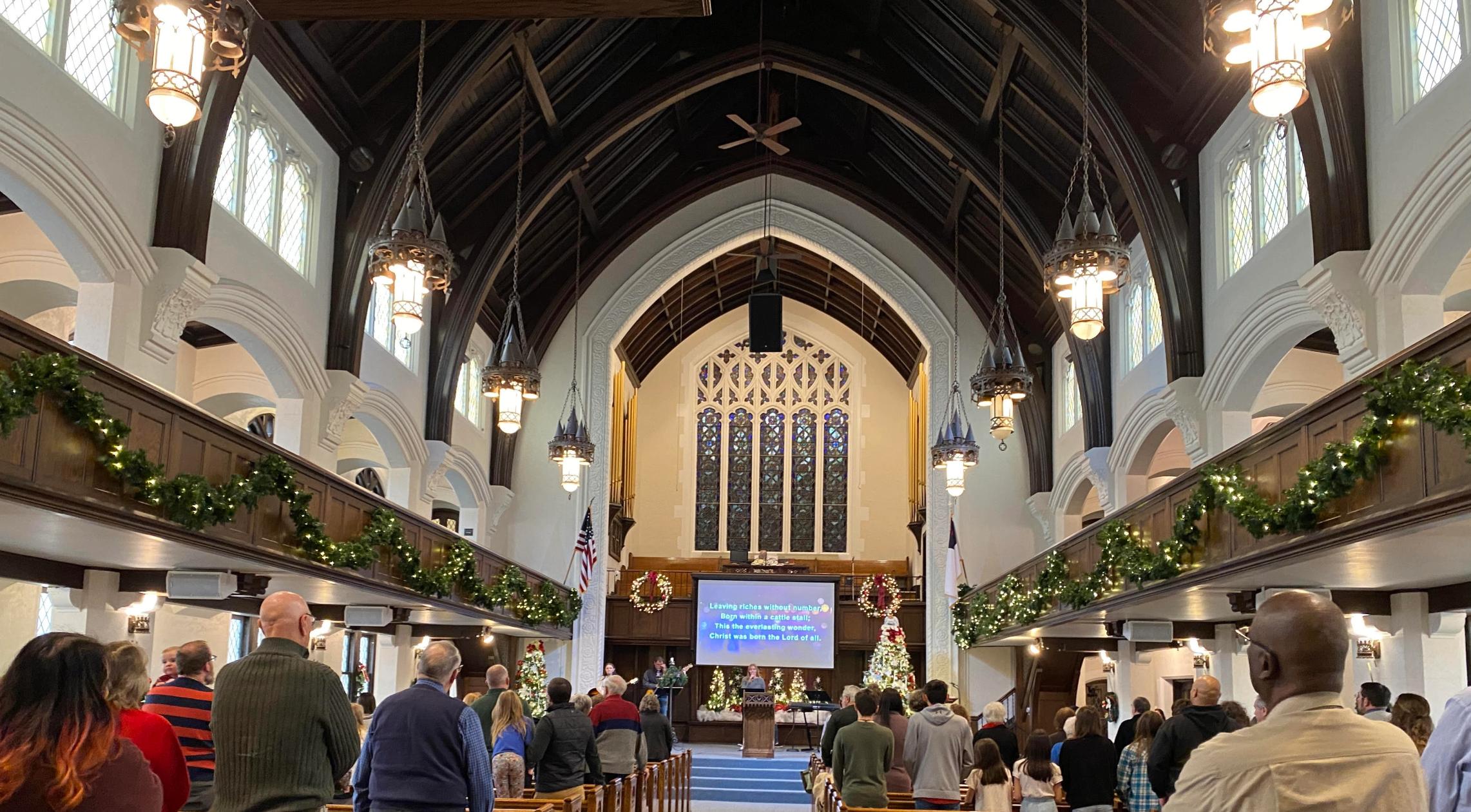 A congregation seated in the sanctuary decorated for Christmas, a screen at the front showing the service.