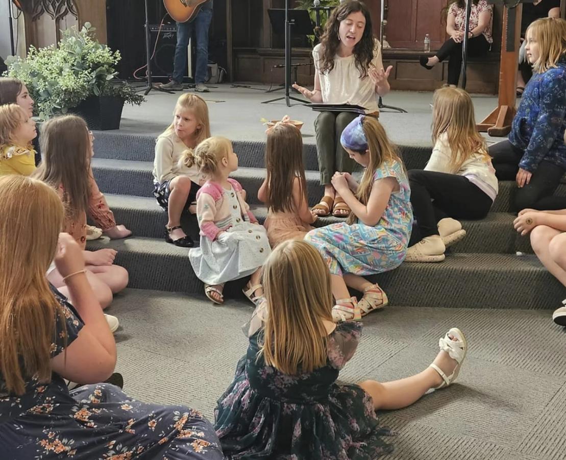 A leader tells a story to children sitting on carpeted steps