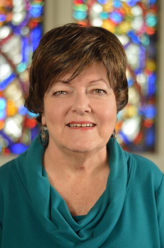 Molly Flodder smiling in a teal top, a stained glass window behind her.