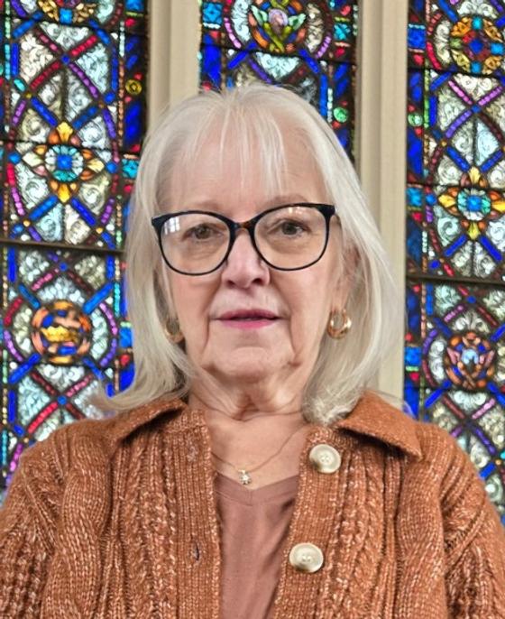 Sally Butler, an older woman with glasses, in front of a stained glass window.