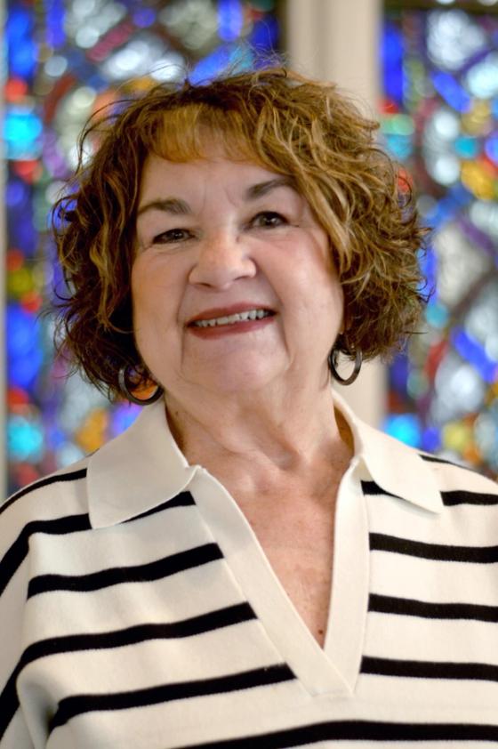 Cheryl Flaherty smiling in a striped top, a stained glass window behind her.