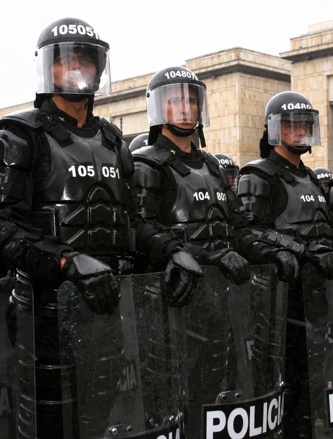 Uniformados antidisturbios con cascos, protección corporal y escudos policiales.