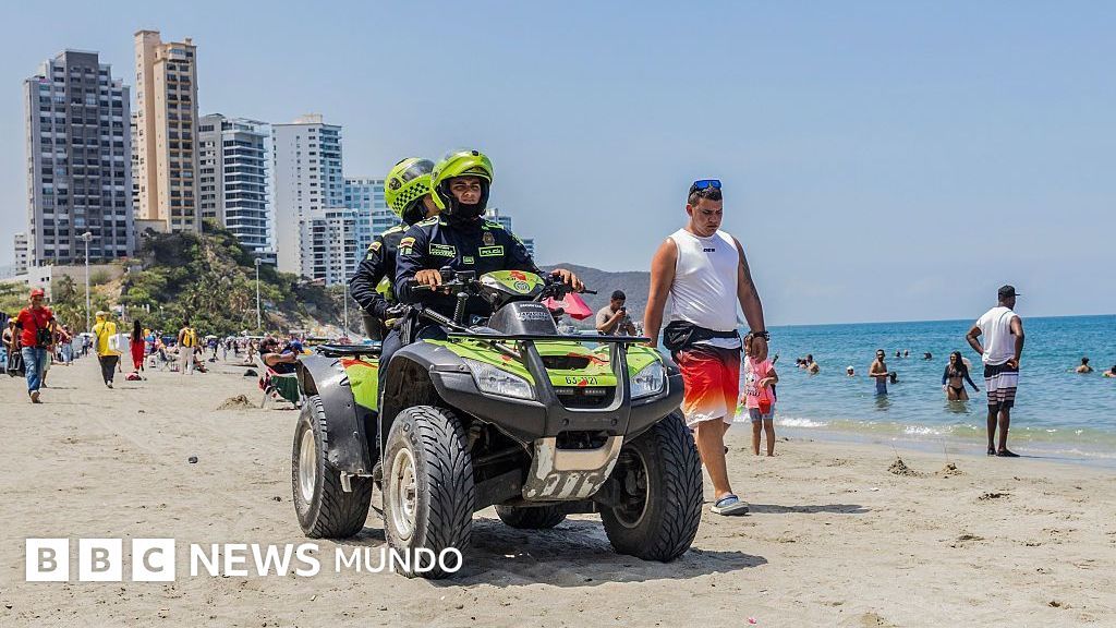 Policías patrullan en cuatrimoto una playa de Santa Marta mientras bañistas caminan por la orilla.