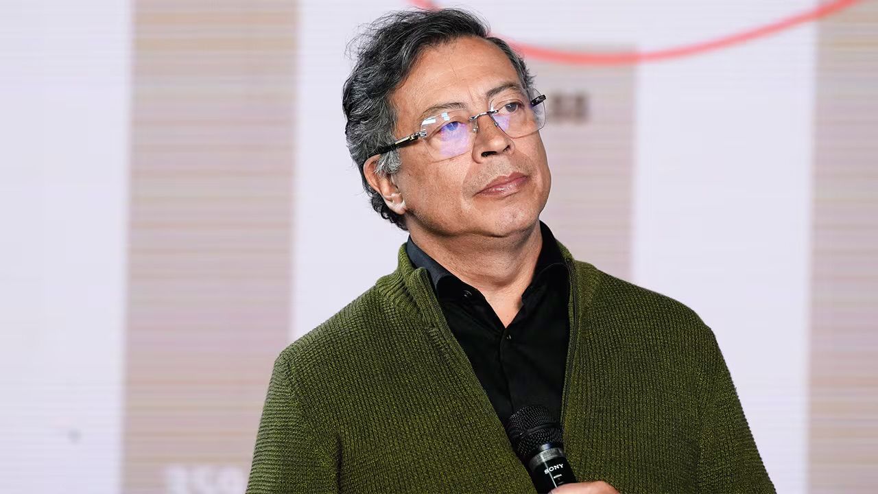 Gustavo Petro con gafas y saco verde sostiene un micrófono.