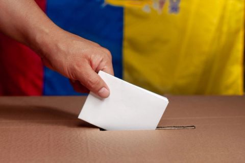 Una persona introduce un voto en una urna con la bandera de Colombia de fondo