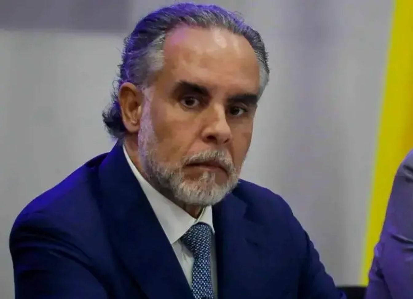 Hombre de cabello canoso y barba con traje azul y corbata.