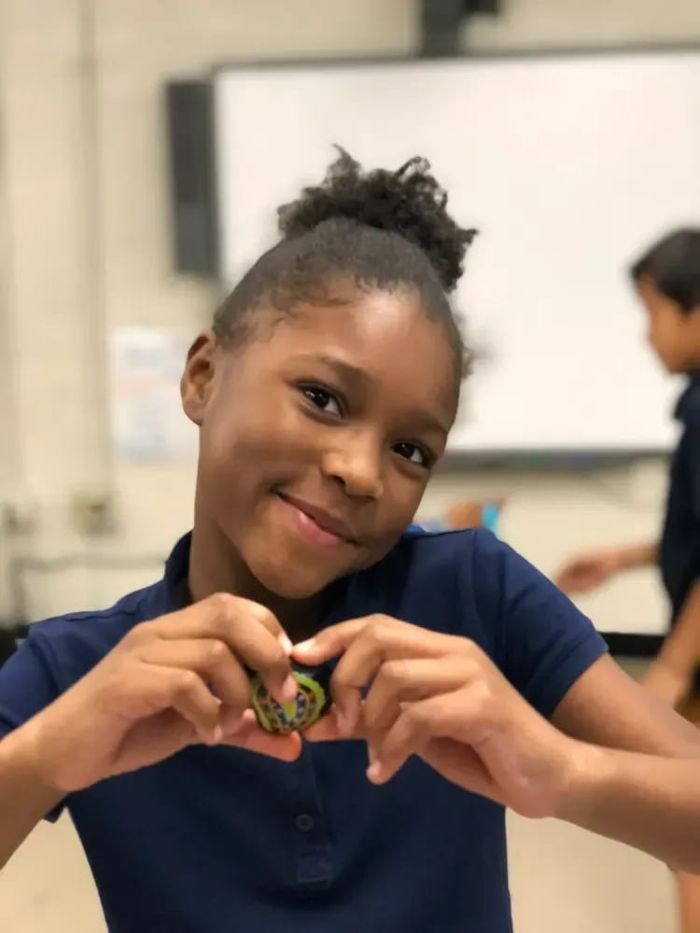 A smiling student making a heart shape with her hands