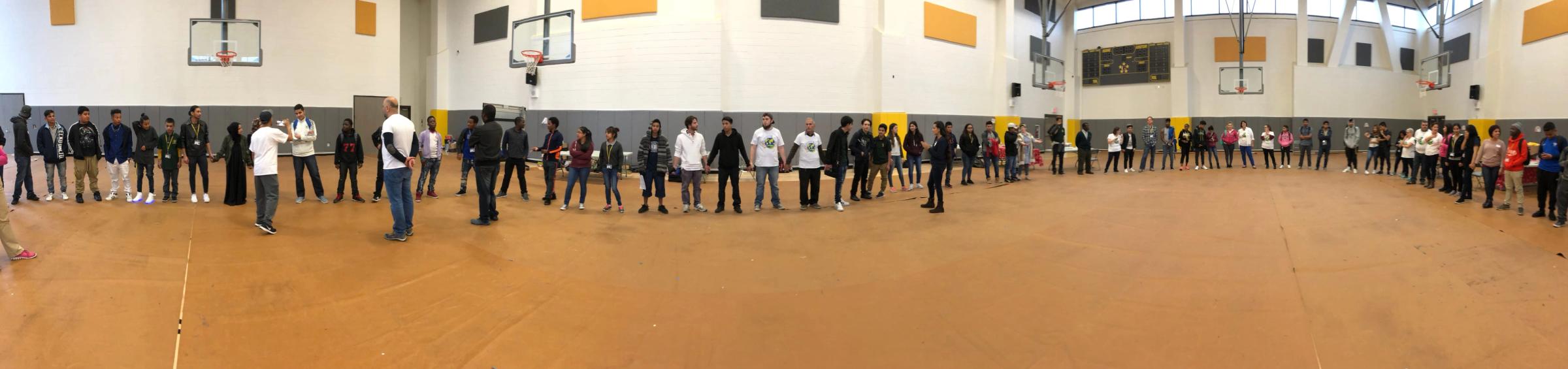 Young people and facilitators holding hands in a large circle in a school gym