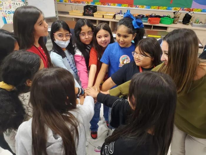 Students and a facilitator stacking their hands together in a huddle