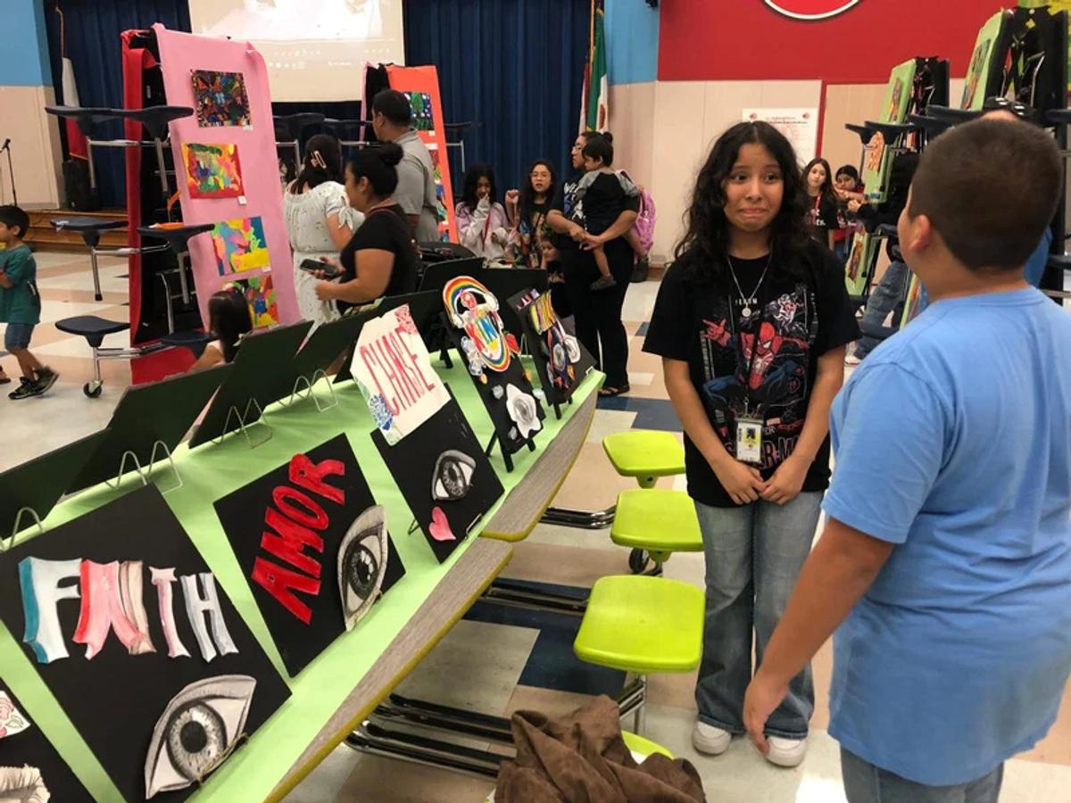 A student presenting her artwork to families at the end of the school year