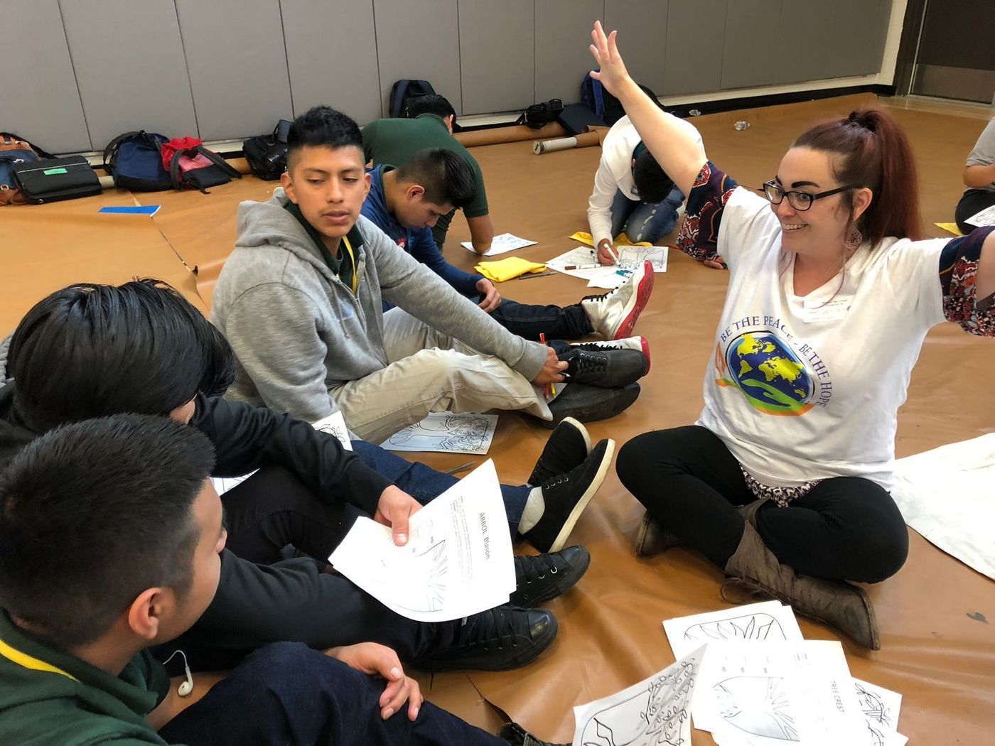 A facilitator leading a drawing activity with teenagers sitting on the floor