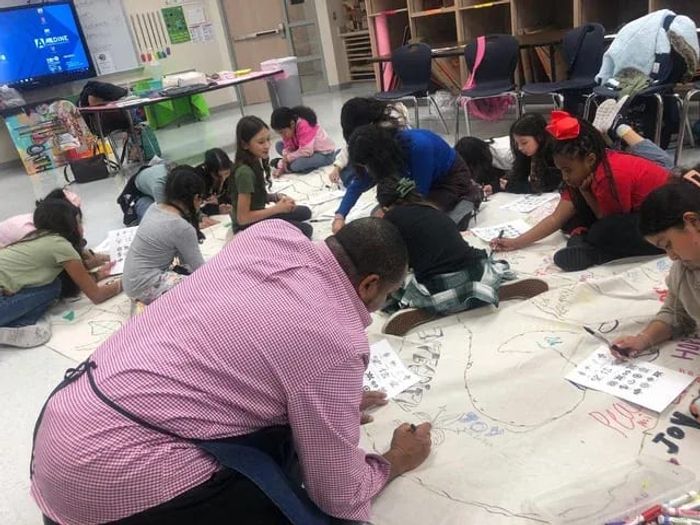 Students and a facilitator drawing together on a large banner on the floor