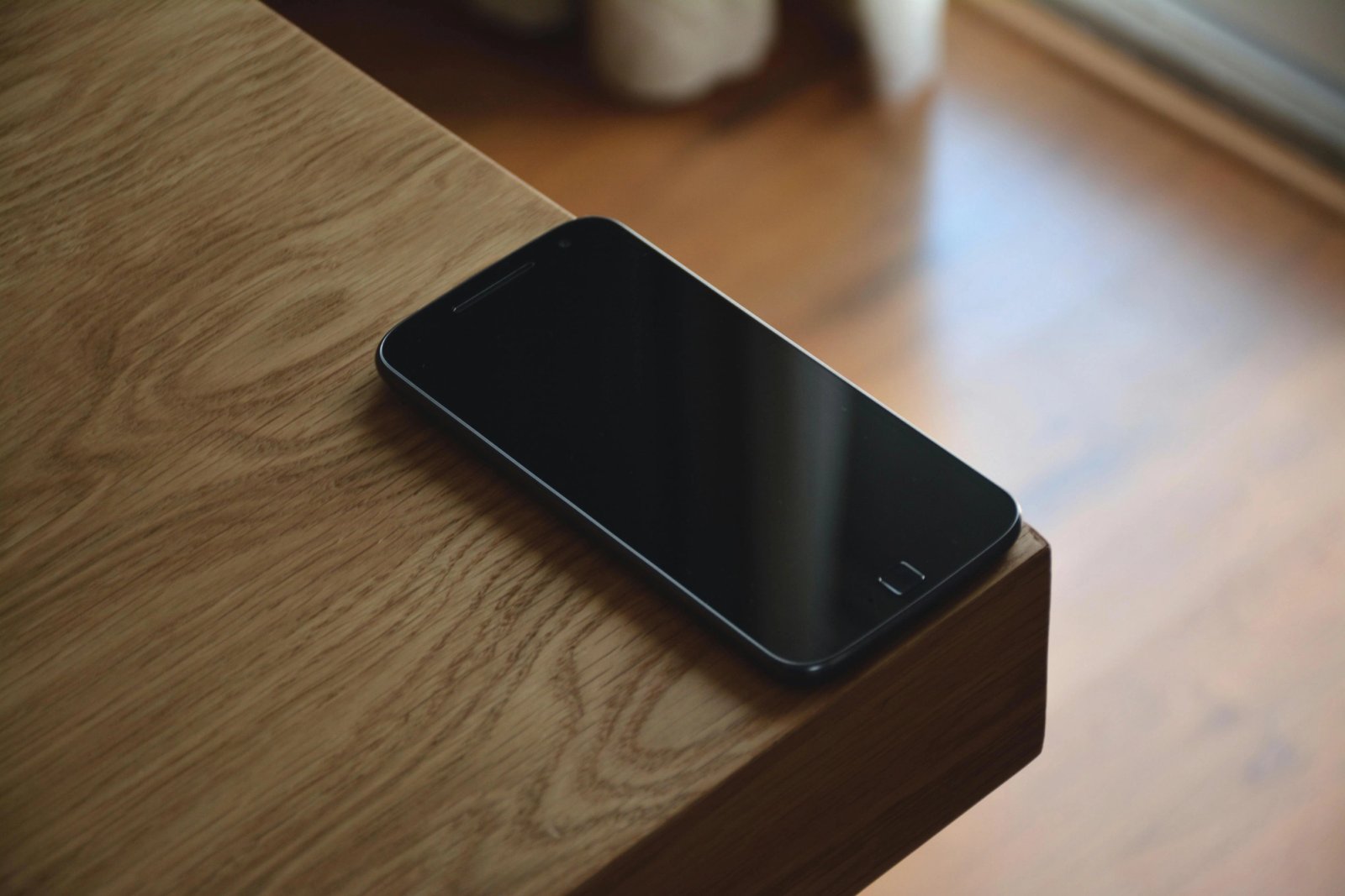 Teléfono móvil con pantalla apagada sobre el borde de una mesa de madera