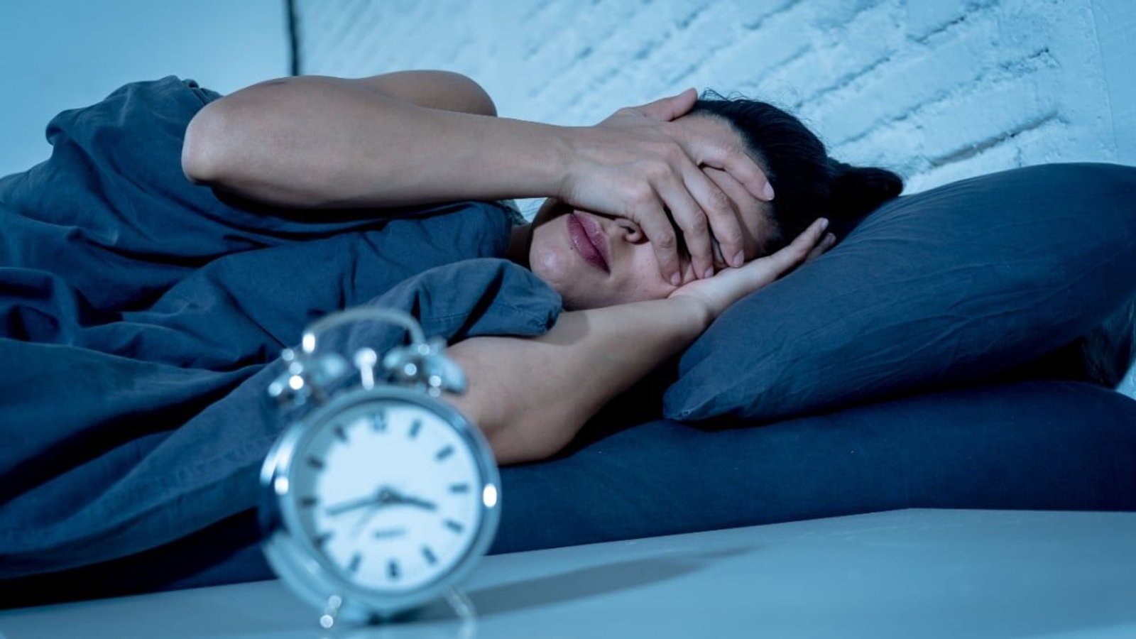Mujer en cama mirando el reloj con expresión de cansancio e insomnio.