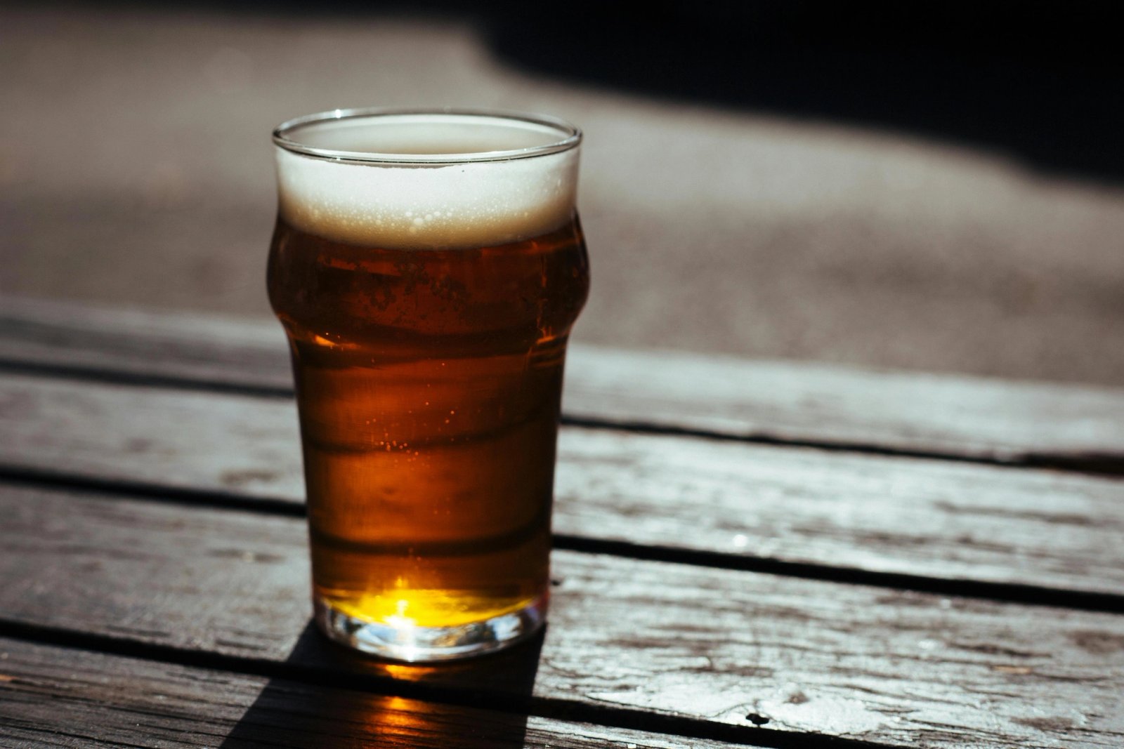 Vaso de cerveza ámbar sobre una mesa de madera desgastada, iluminado por la luz del atardecer.