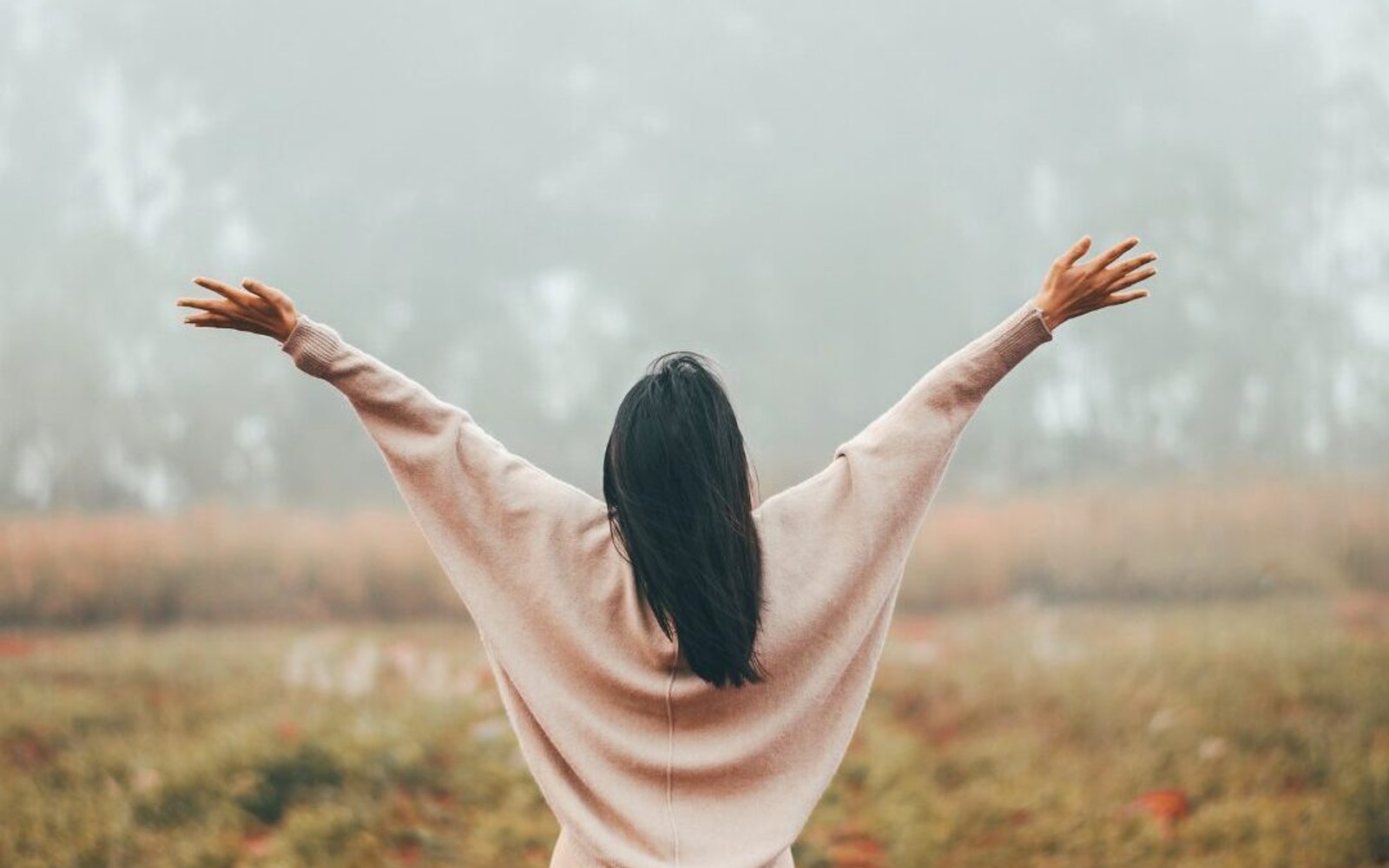Mujer en exterior con los brazos alzados, expresando bienestar y vitalidad.