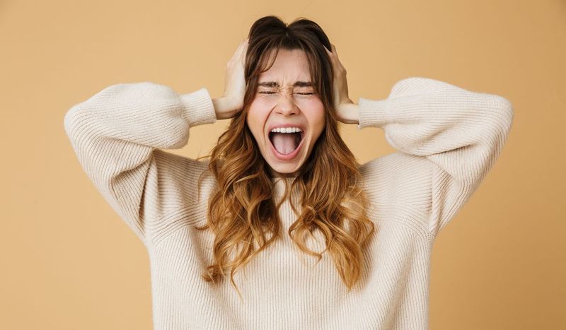 Joven cansada y frustrada por la hiperexigencia emocional contemporánea, con la cabeza apoyada en la mano.