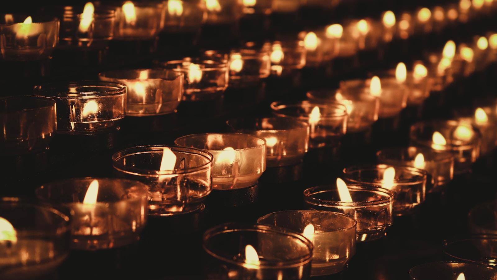 Fileiras de velas votivas acesas em copos de vidro, no escuro