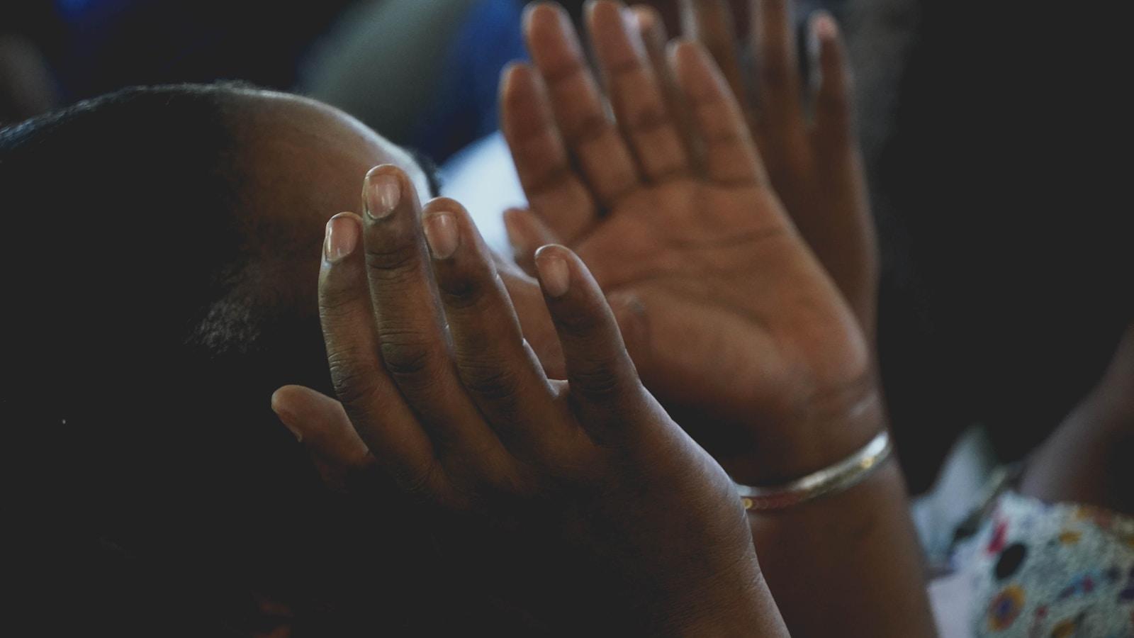 Mulher com as mãos erguidas diante do rosto, em oração