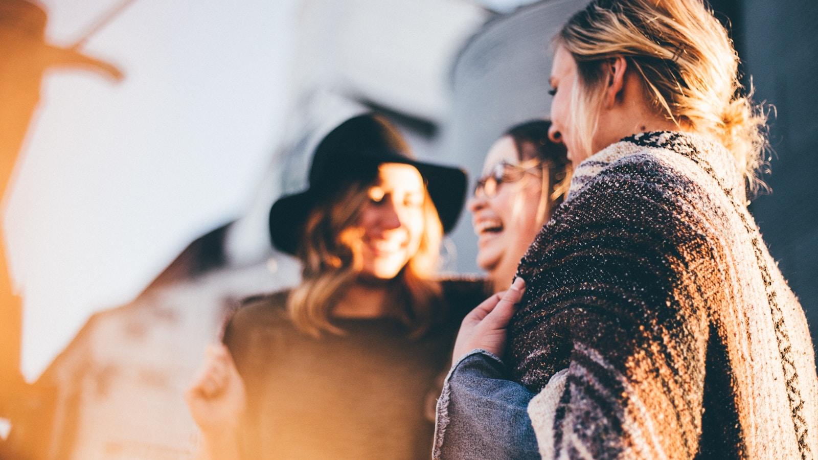 Três amigas conversando e rindo ao sol, em close