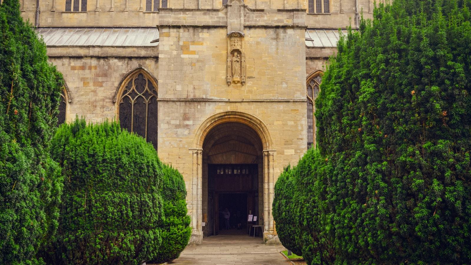 Entrada em arco de uma igreja de pedra, entre dois arbustos podados