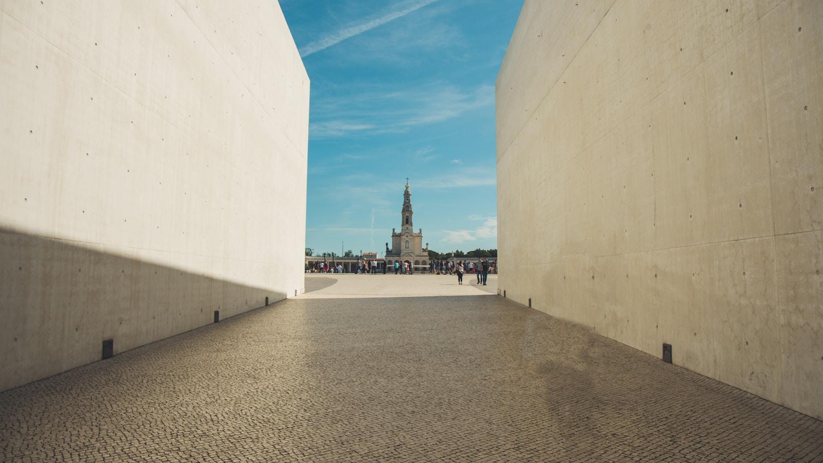Esplanada do Santuário de Fátima, com a torre da Basílica ao fundo, vista entre dois muros de concreto