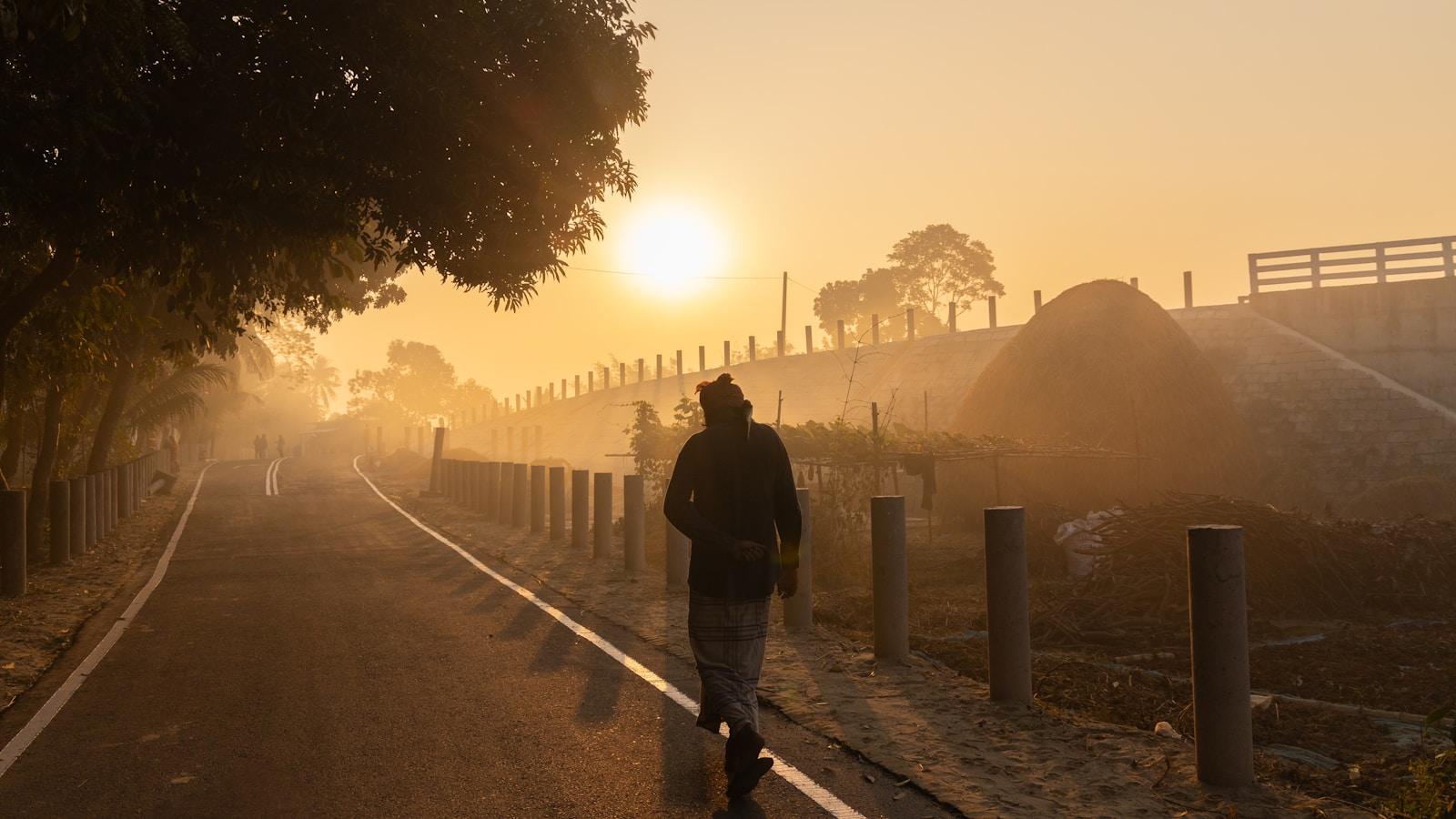Pessoa caminhando por uma estrada com névoa ao nascer do sol