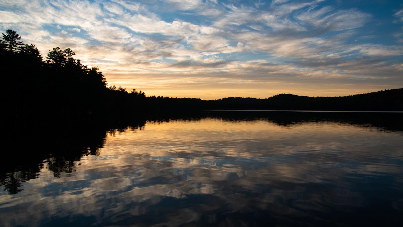 Nuvens ao pôr do sol refletidas num lago tranquilo, entre árvores