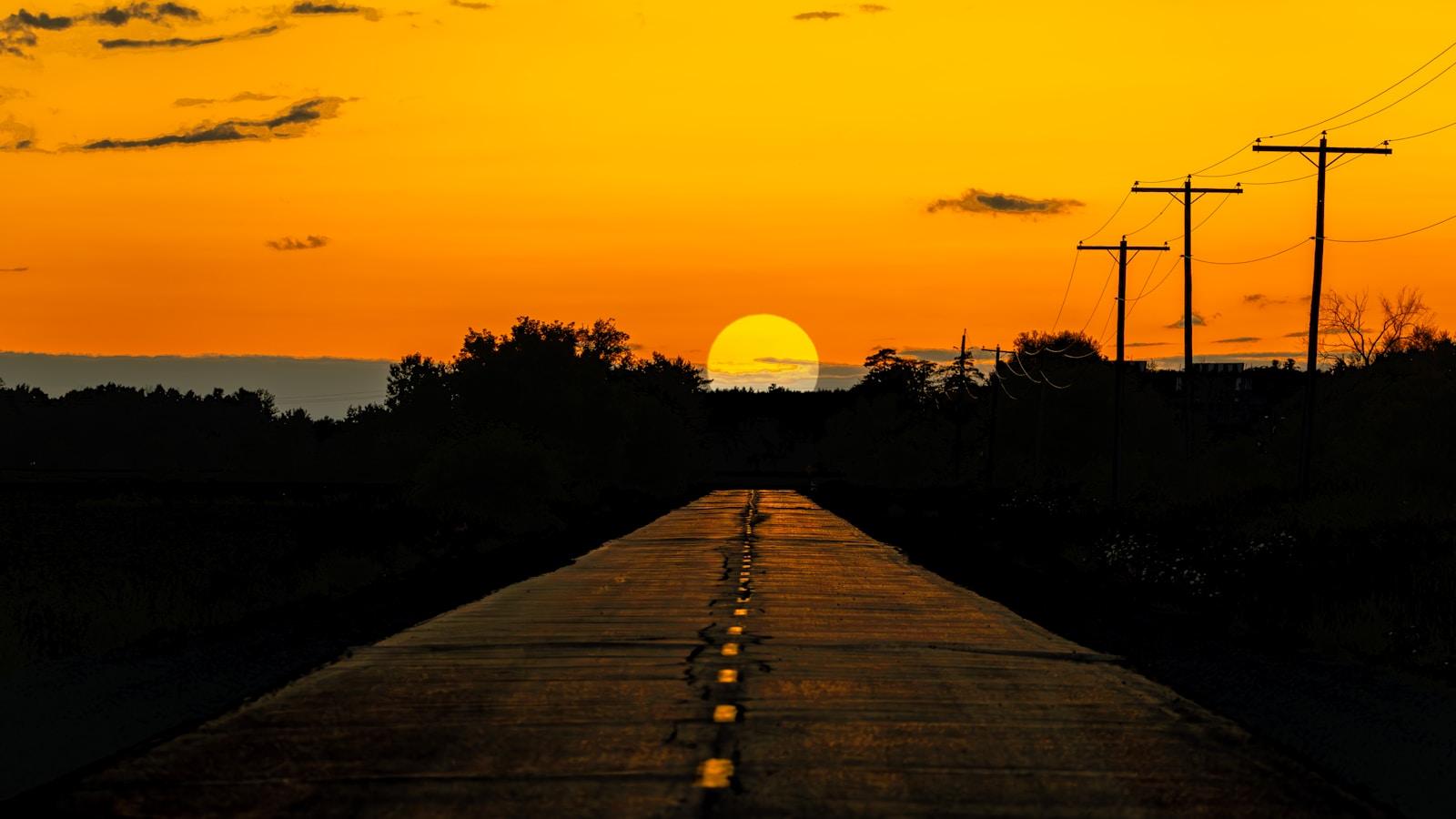 Estrada reta em direção ao sol poente, com postes ao lado