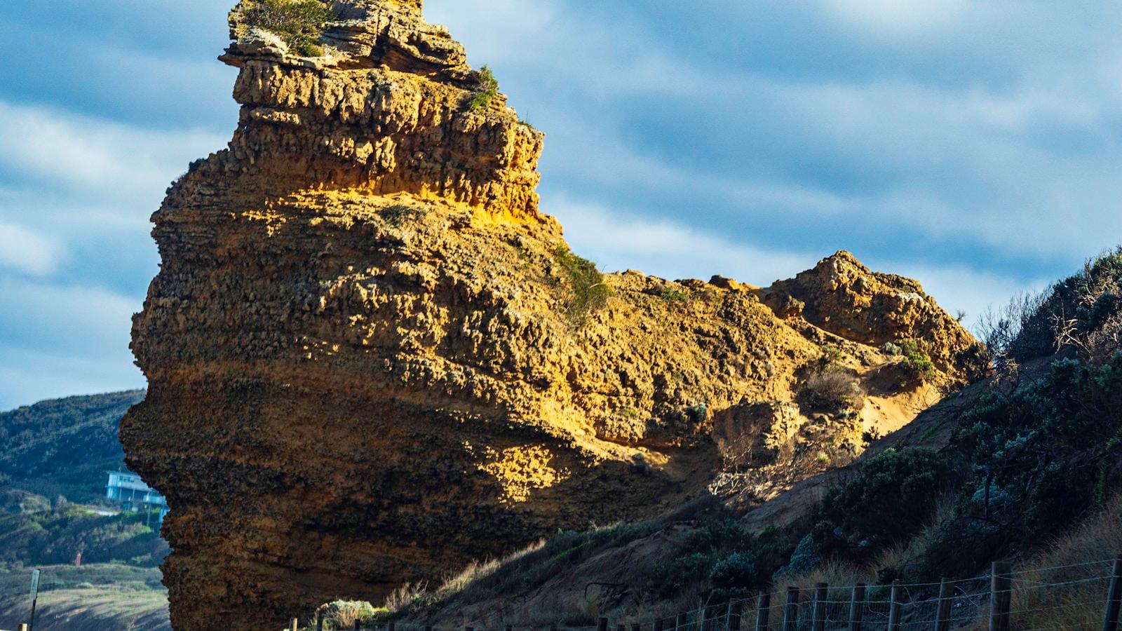 Grande formação rochosa amarelada erguendo-se sobre a encosta, sob céu nublado