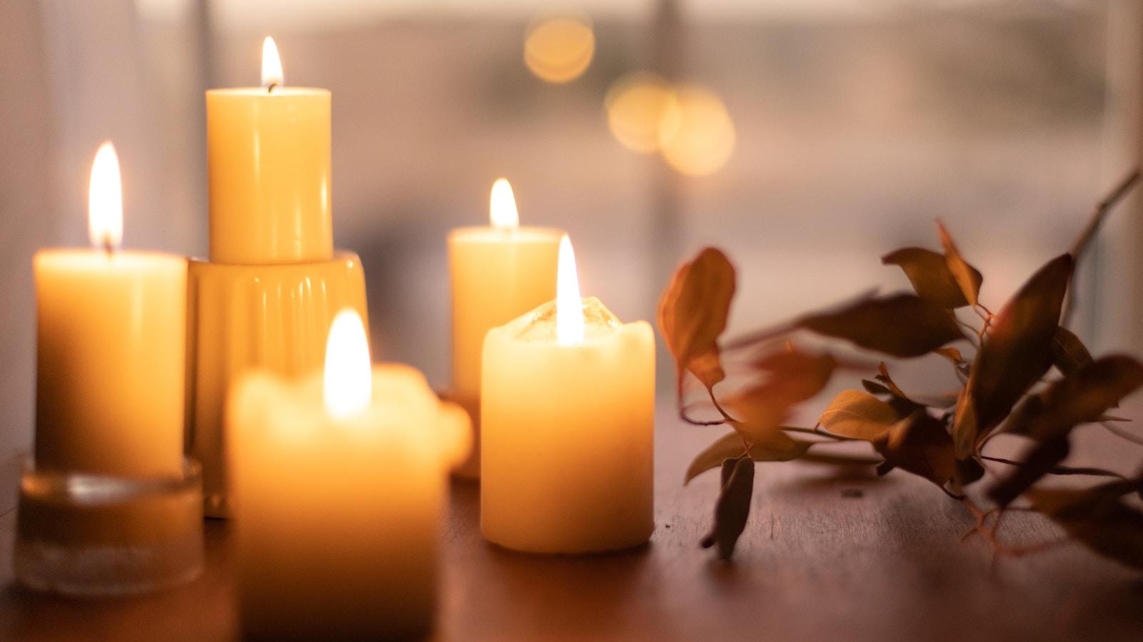 Várias velas acesas de tamanhos diferentes sobre uma mesa, com folhas secas ao lado