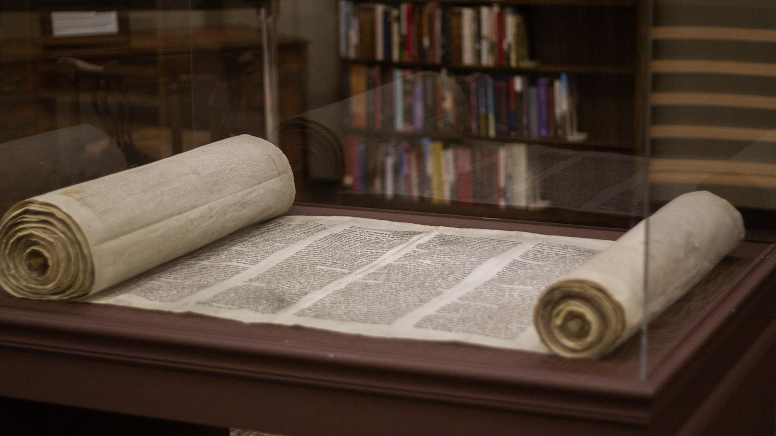 Rolo da Torá aberto numa vitrine, com estantes de livros ao fundo