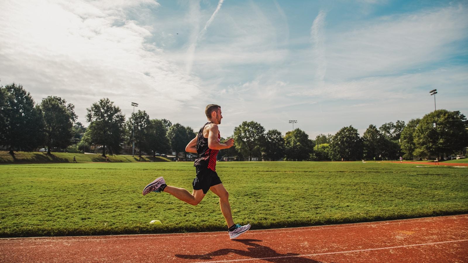 Corredor em plena passada numa pista de atletismo, com gramado e árvores ao fundo