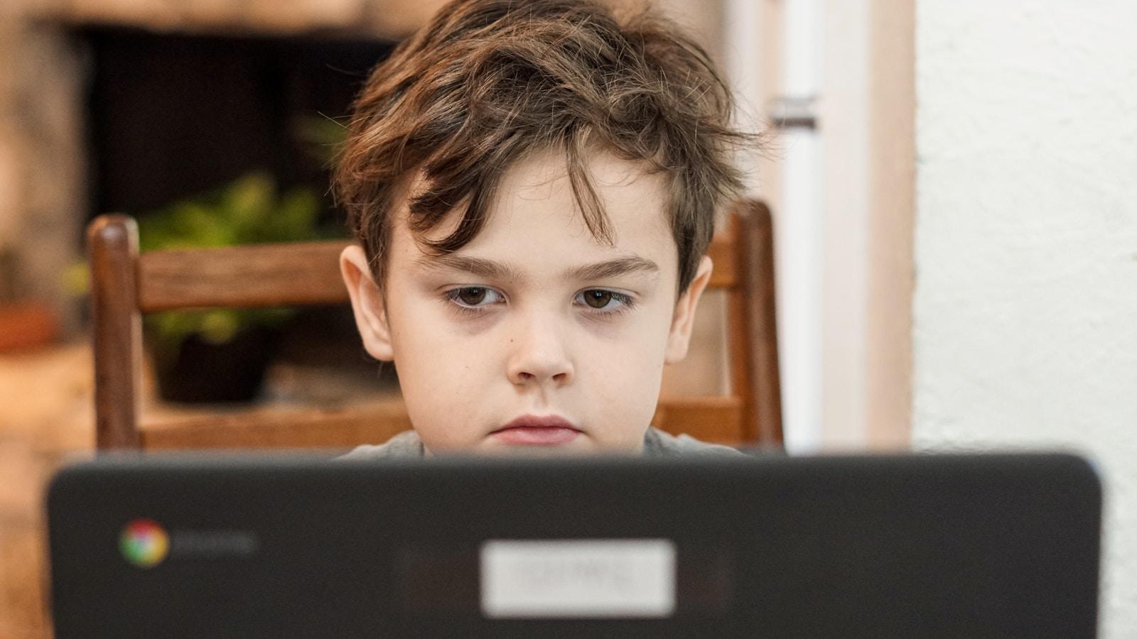 Menino olhando concentrado para a tela de um laptop