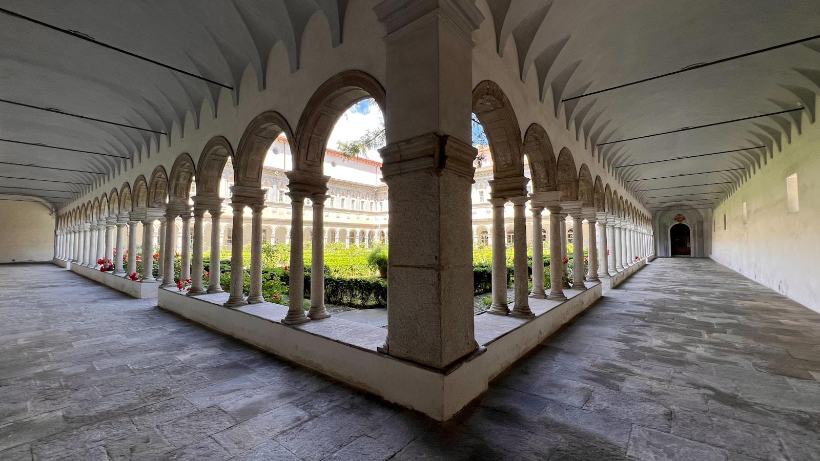 Claustro de mosteiro com arcos de pedra em volta de um jardim