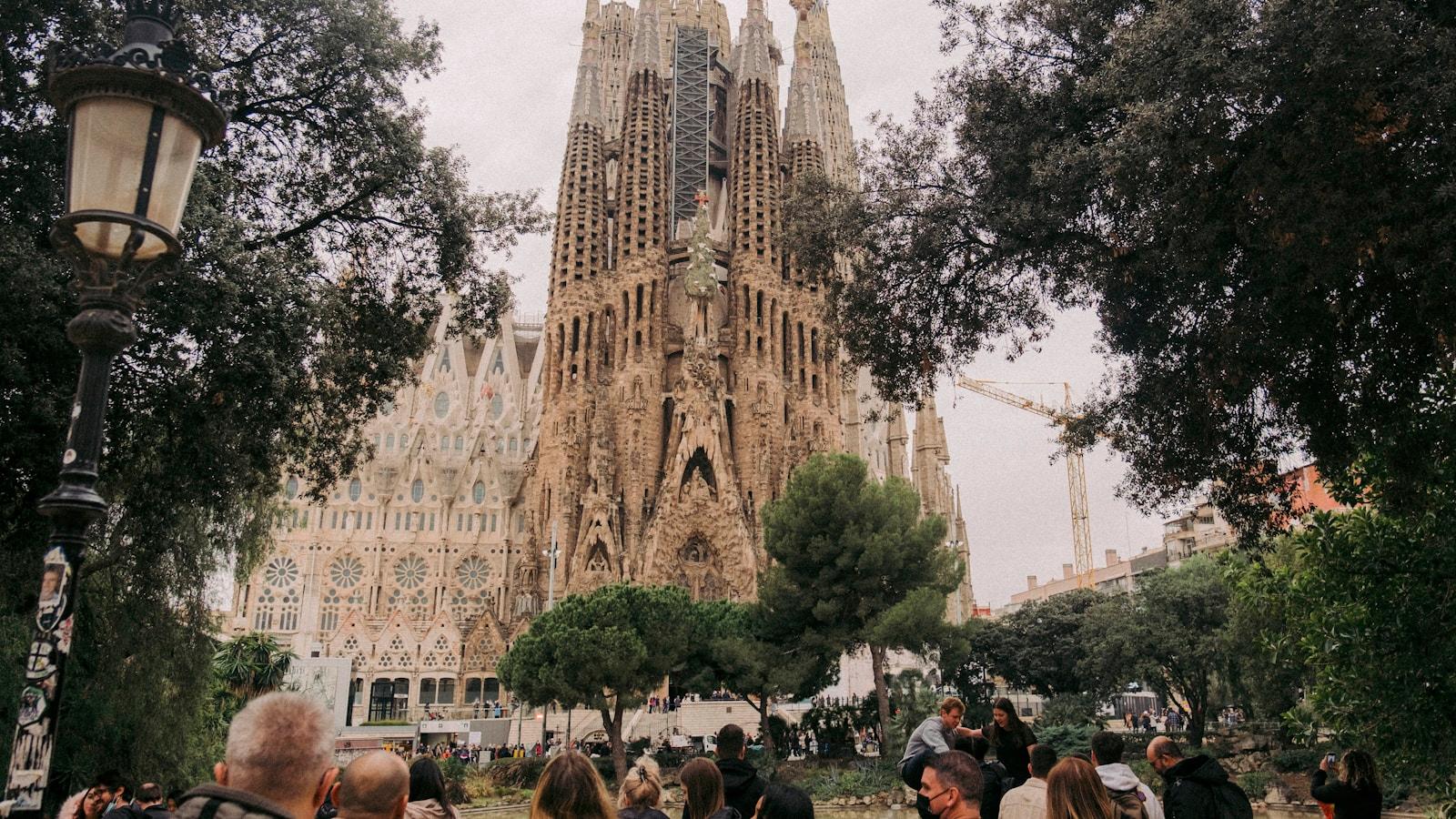 Fachada da Sagrada Família, em Barcelona, vista da praça com árvores e visitantes