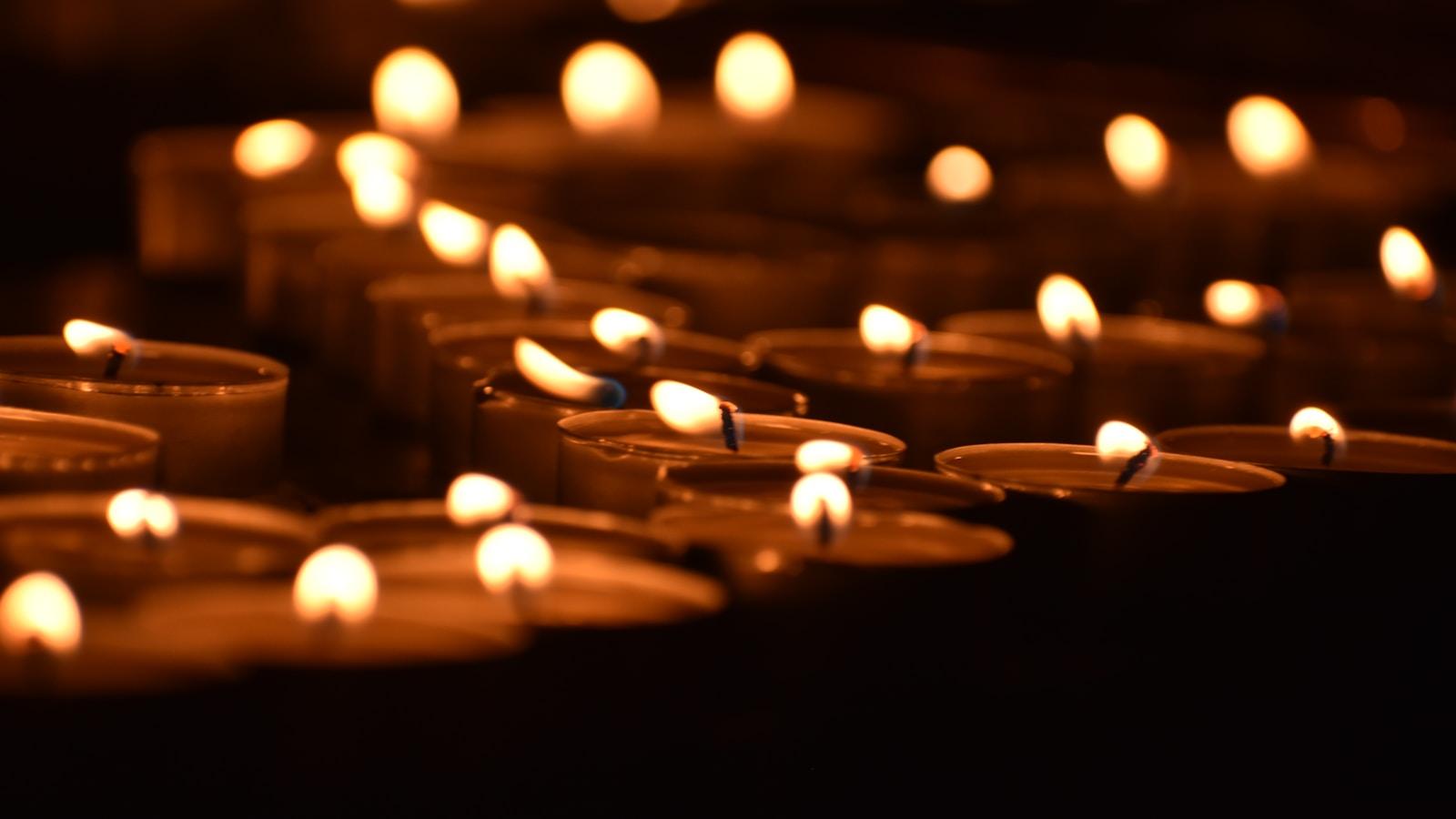 Velas votivas acesas em fileiras, com chamas desfocadas ao fundo