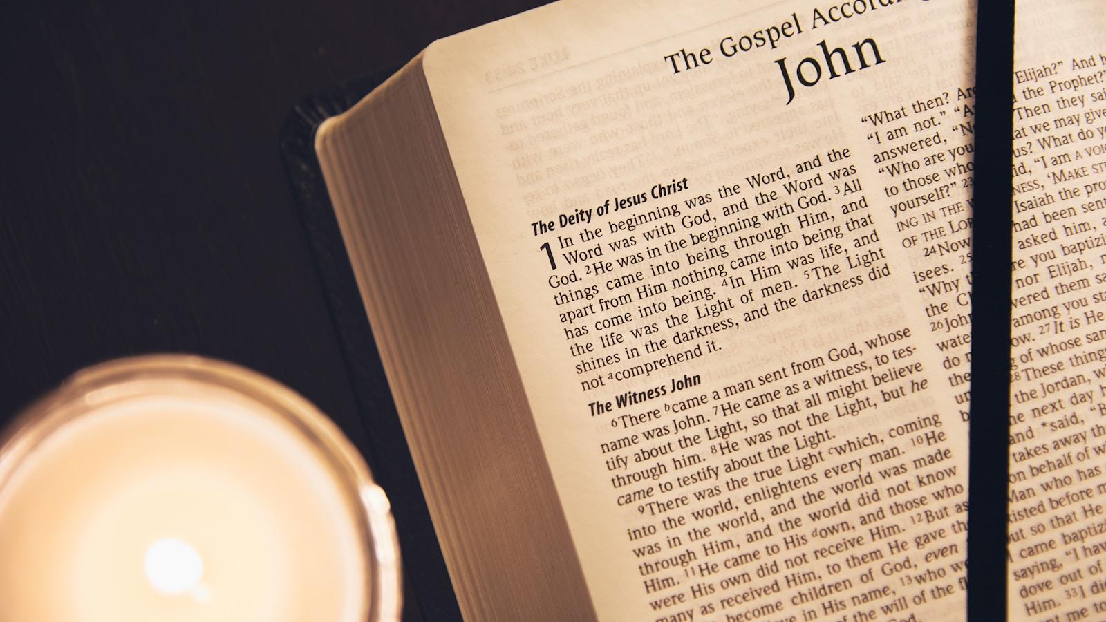 Bíblia aberta no Evangelho de João, com uma vela acesa ao lado