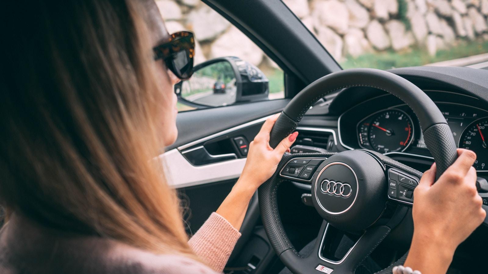 Mulher ao volante de um carro, com óculos escuros, vista de trás