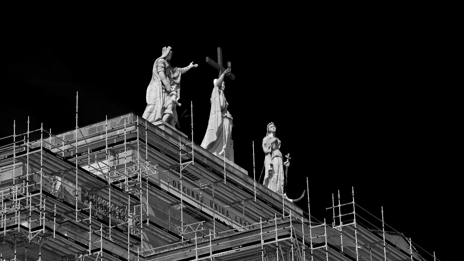 Estátuas no alto de uma igreja cercadas por andaimes, em preto e branco