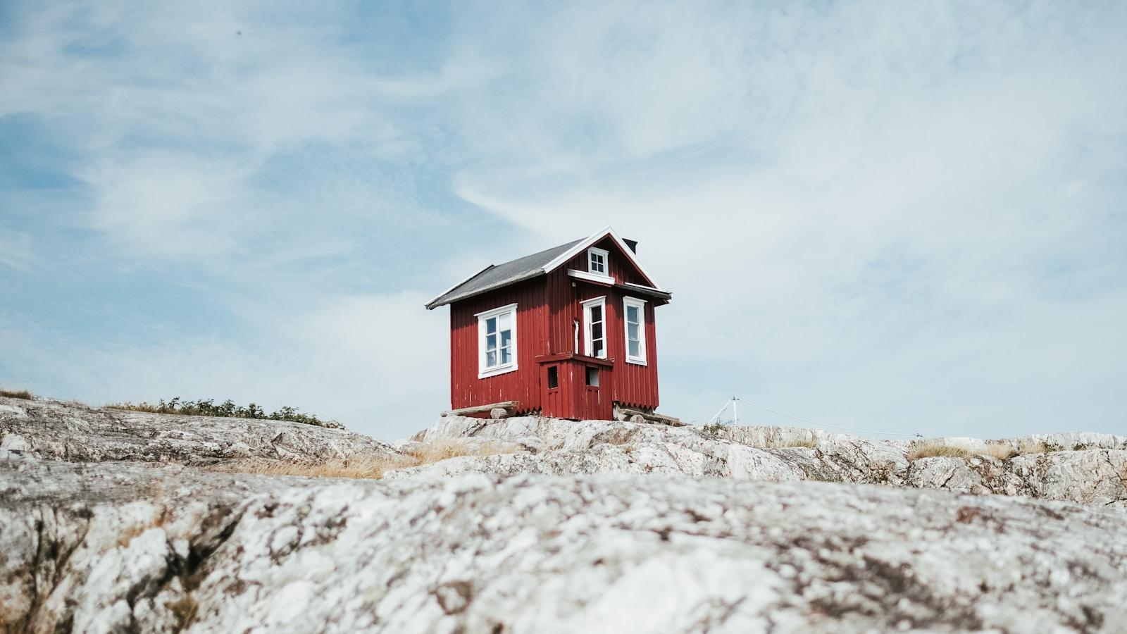 Pequena casa vermelha de madeira construída sobre uma rocha, sob céu claro