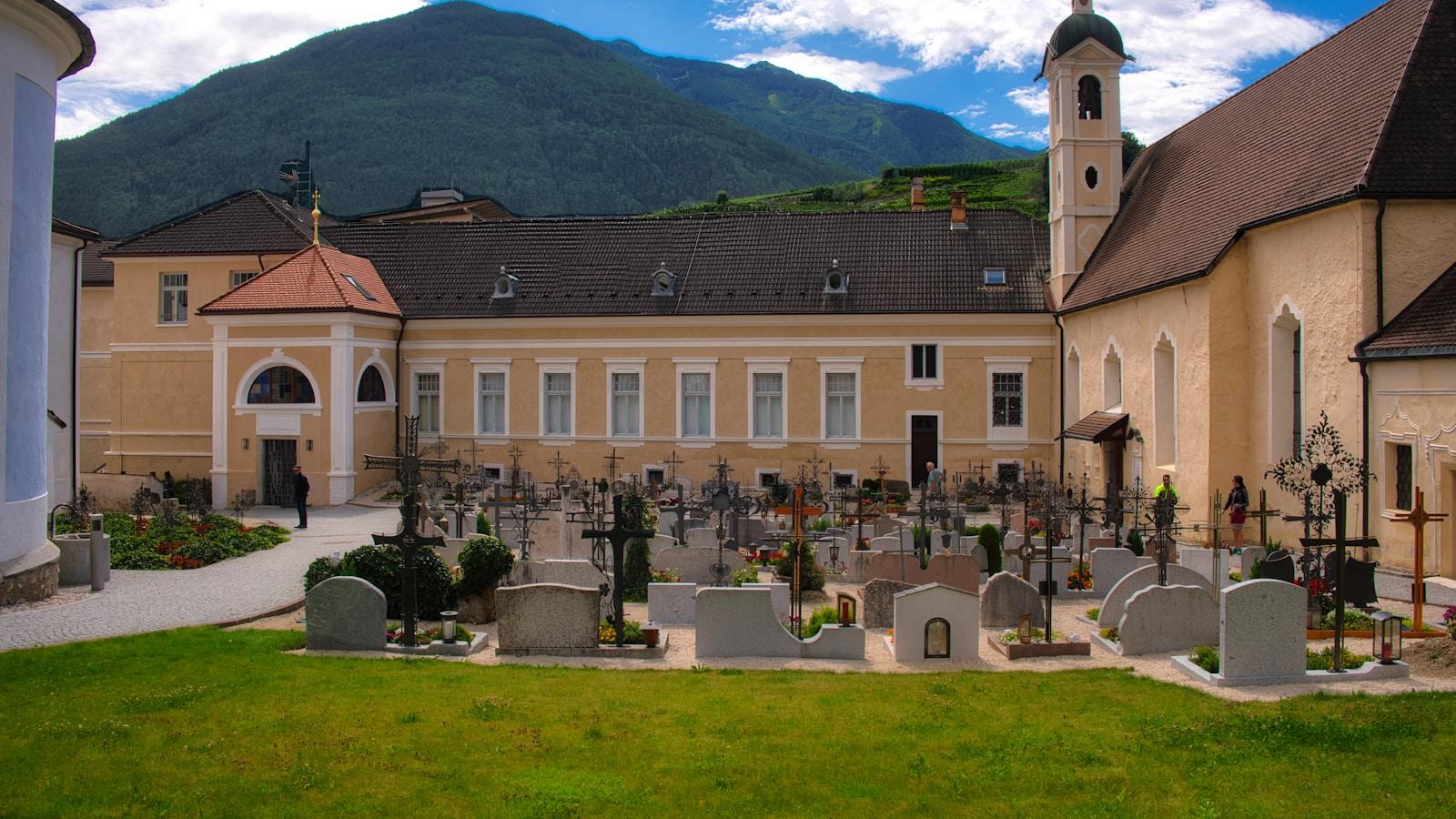 Cemitério com cruzes de ferro no pátio de um mosteiro, com igreja e montanhas ao fundo